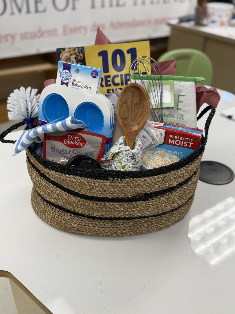 photo of a basket full of baking related accessories such as reusable cupcake cups, boxes of mix, a wooden spoon, whisk, and recipe book