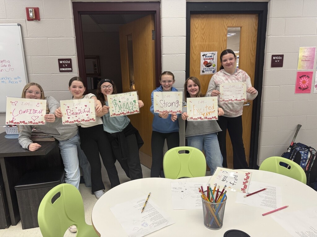Students for the lean-in girls program posing with signs like "confident" "beautiful" "strong" "excited" and more.