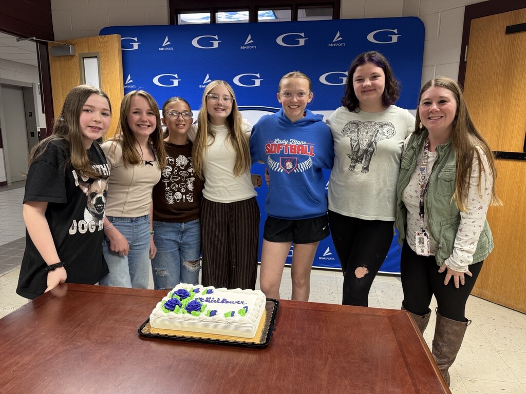 students in front of a cake that says "girl power" with Mrs. Sponaugle