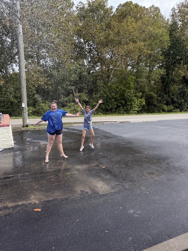 students standing in the parking lot with their arms up waving down cars
