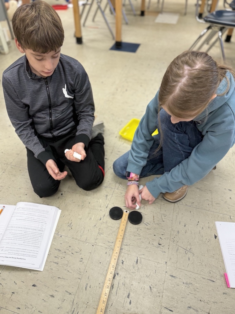 students with two air hockey pucks about to measure distance traveled