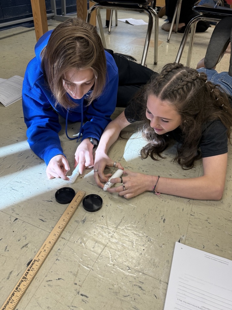 students with two air hockey pucks about to measure distance traveled