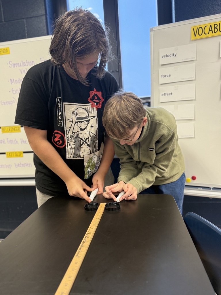 students with two air hockey pucks about to measure distance traveled