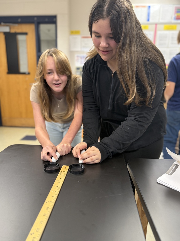 students with two air hockey pucks about to measure distance traveled