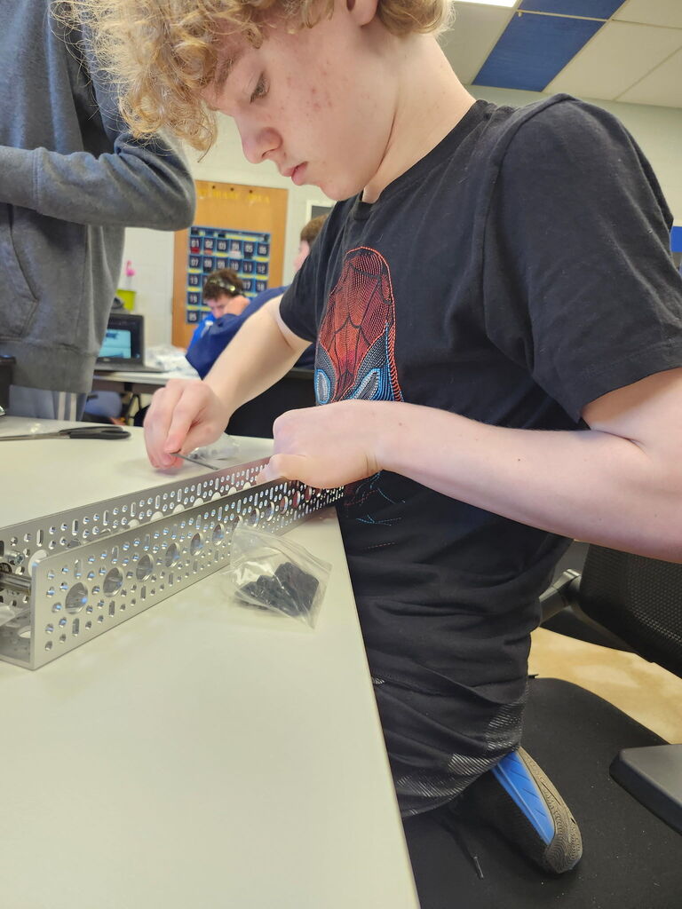 Students working together to assemble and program robots with mechanical tools and laptops.