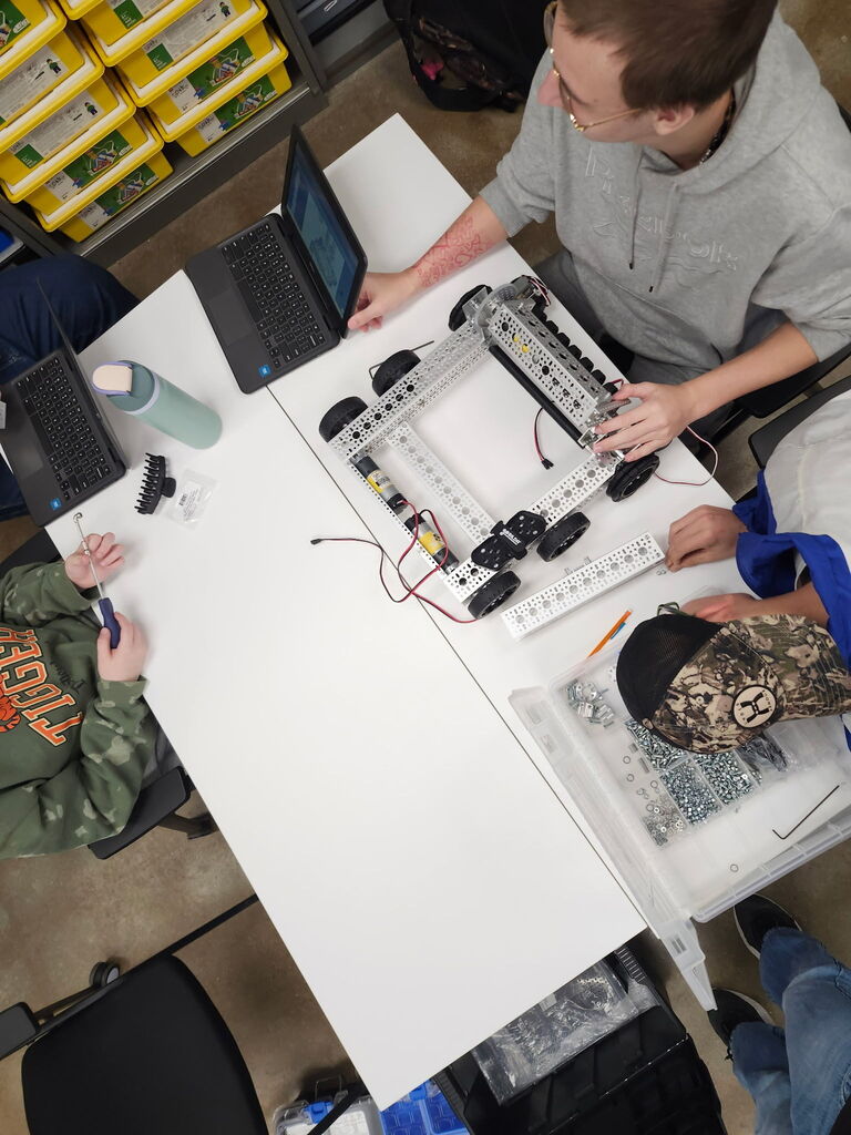 Students working together to assemble and program robots with mechanical tools and laptops.