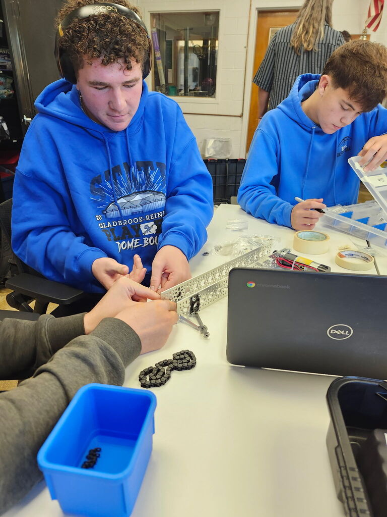 Students working together to assemble and program robots with mechanical tools and laptops.
