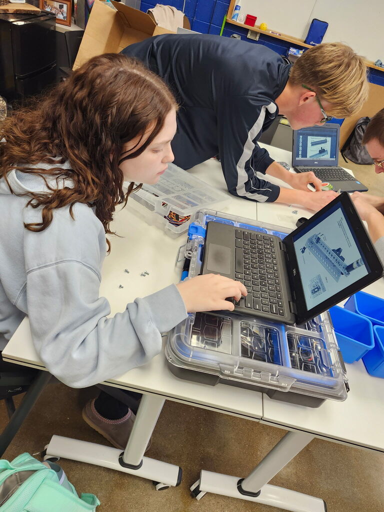 Students working together to assemble and program robots with mechanical tools and laptops.