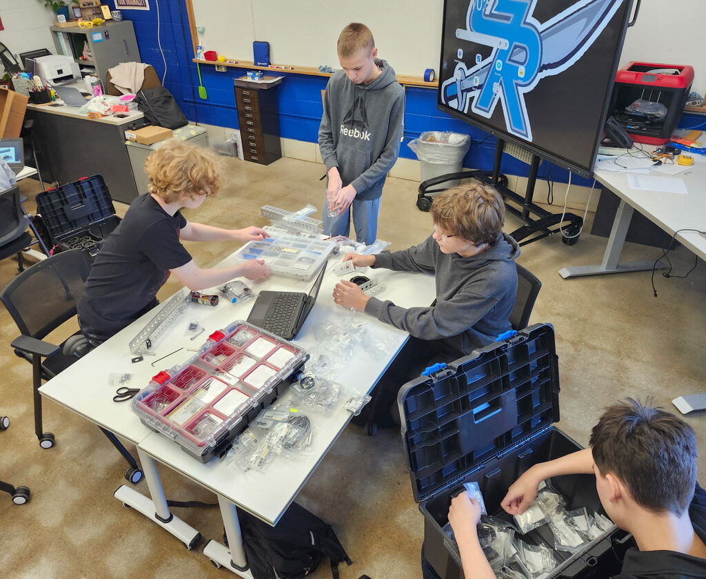 Students working together to assemble and program robots with mechanical tools and laptops.
