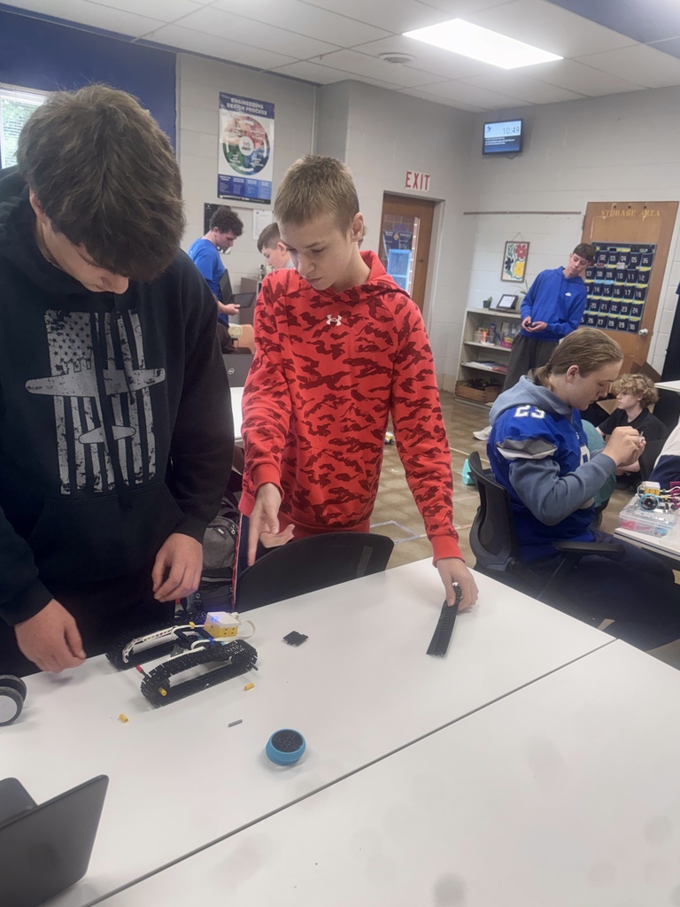 Students working together to assemble and program robots with mechanical tools and laptops.