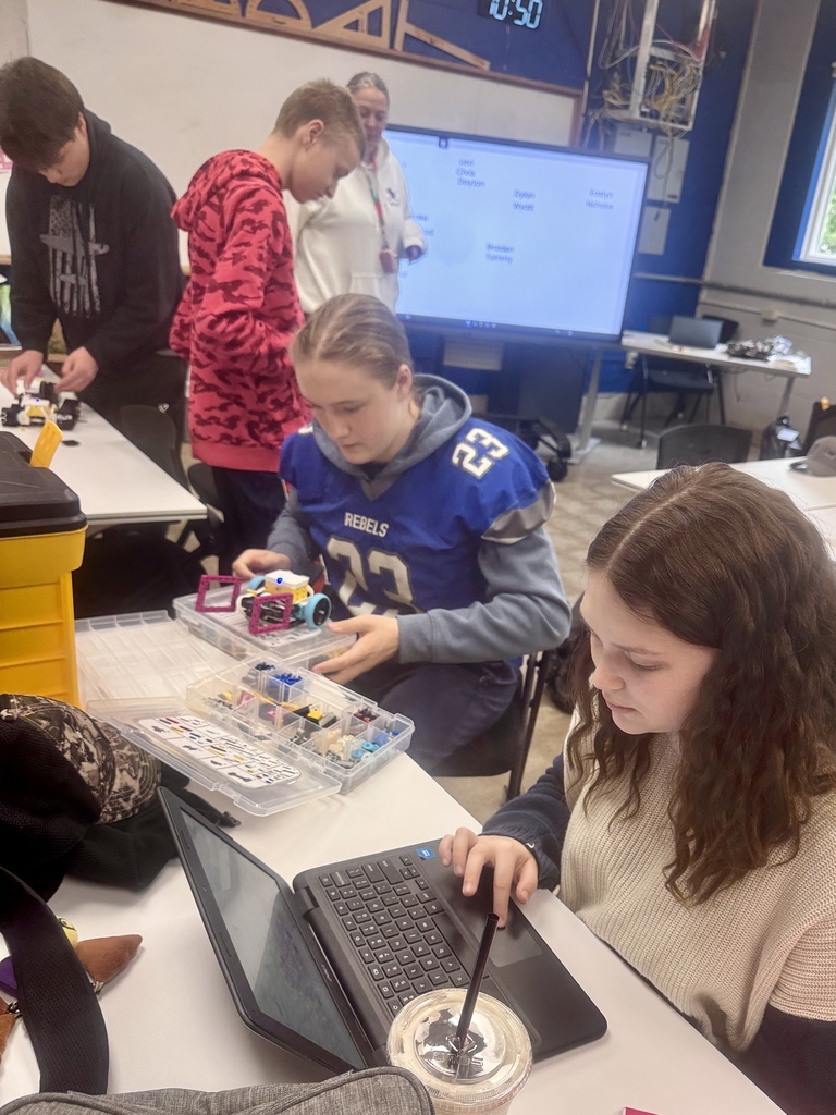 Students working together to assemble and program robots with mechanical tools and laptops.