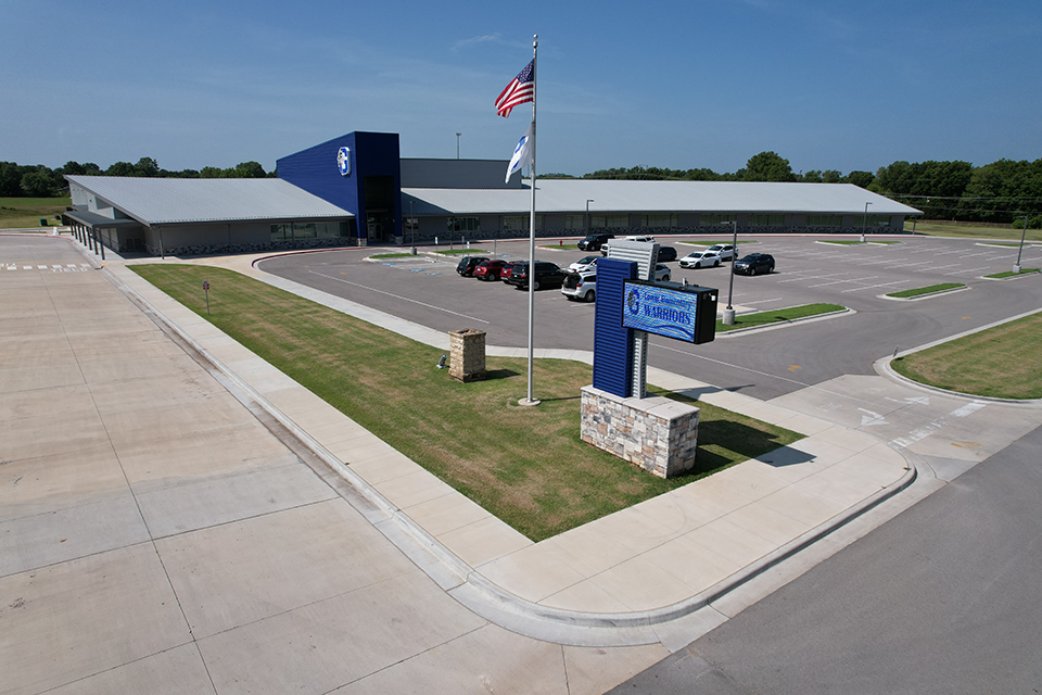An aerial view of a large building with a flagpole in the foreground. The building has an open parking lot.