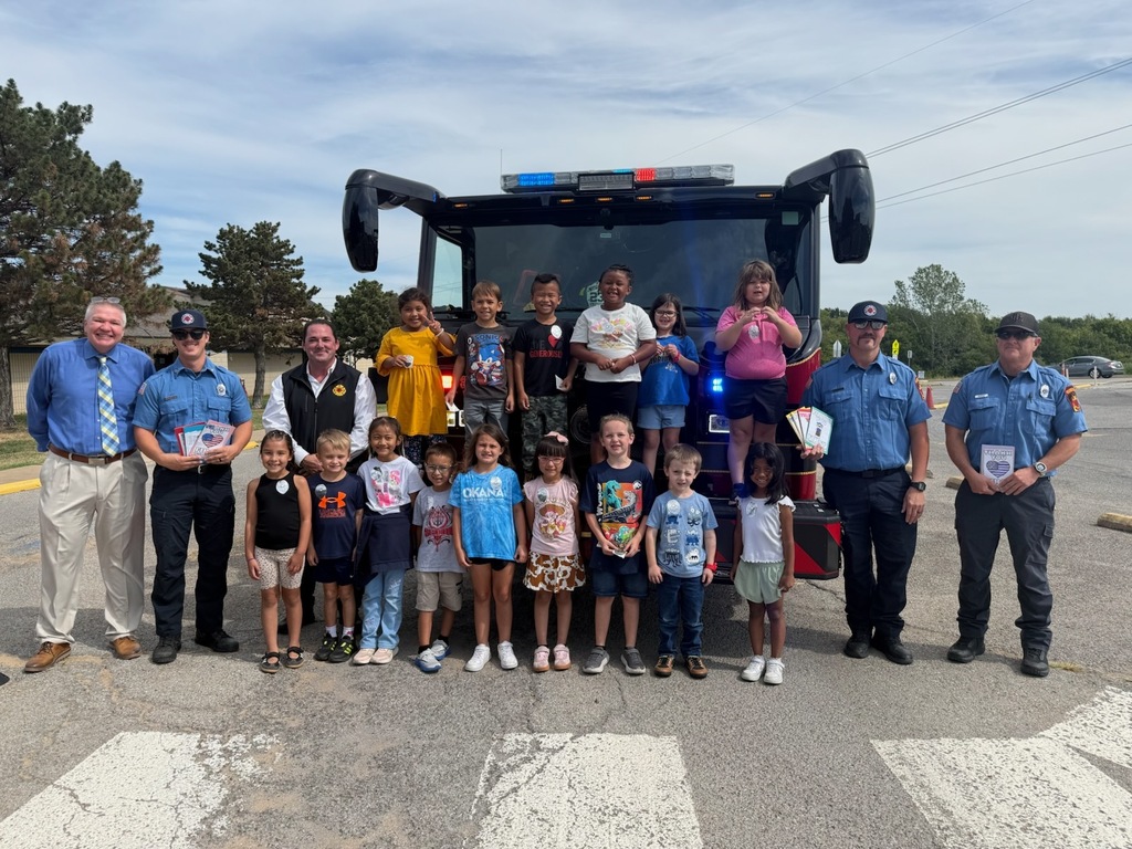 Group of children and adults standing next to a fire truck on a road.
