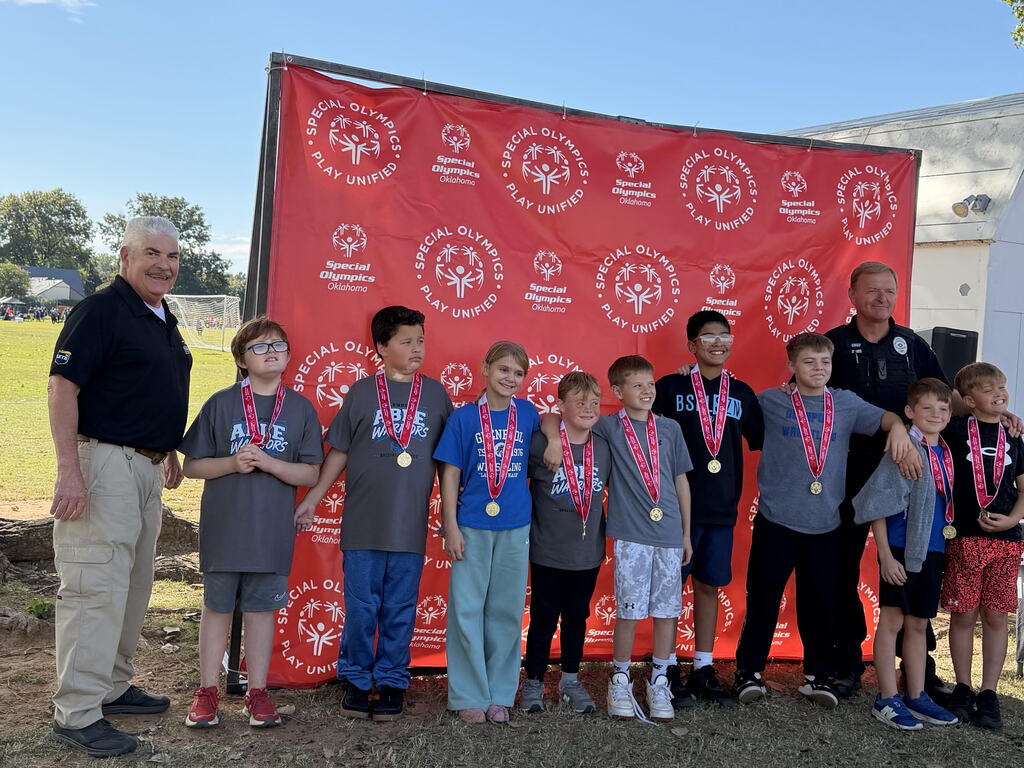 Group of young students wearing medals pose in front of a red banner and two adults.