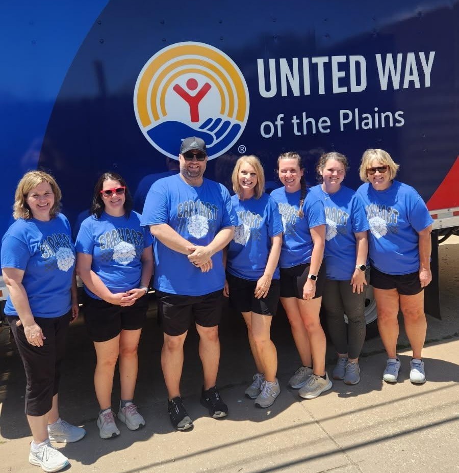 A group of six individuals wearing blue t-shirts stand in front of a United Way of the Plains truck, smiling.