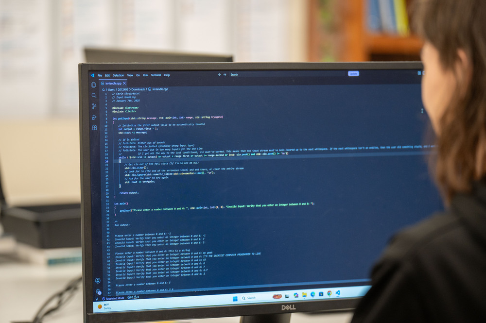 Partial profile of a young man looking at a computer screen displaying lines of code.