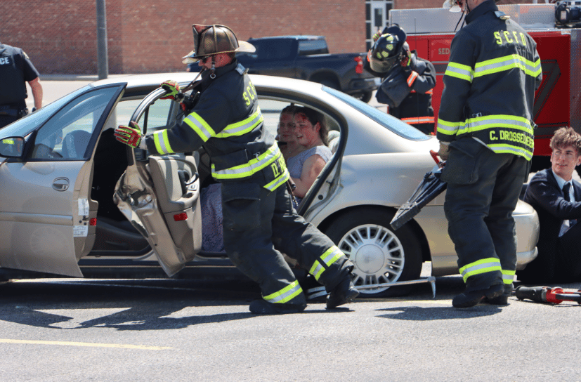 Firefighters demonstrate opening a vehicle with the jaws of life to rescue accident victims in mock DUI demonstration.