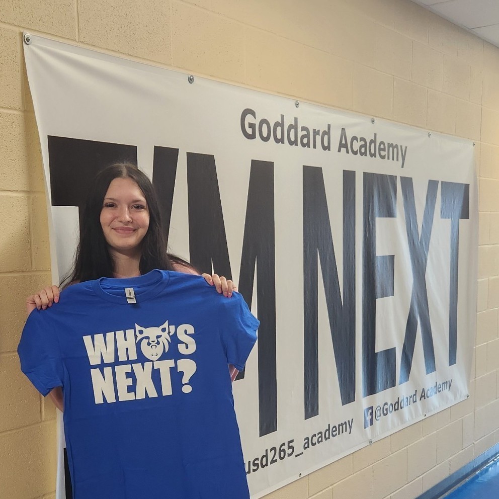 Holding "Who's Next " shirt in front of "I'm Next" banner 