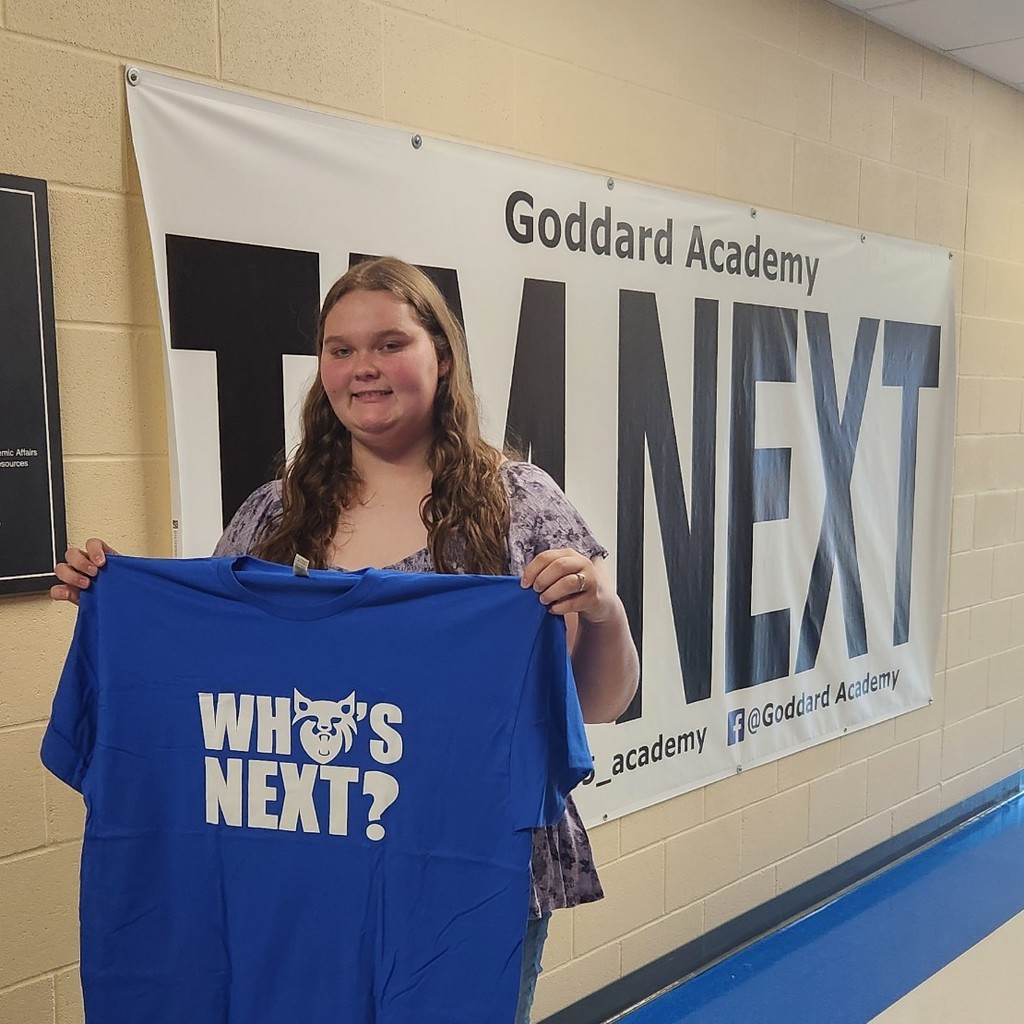 Holding "Who's Next " shirt in front of "I'm next "banner 