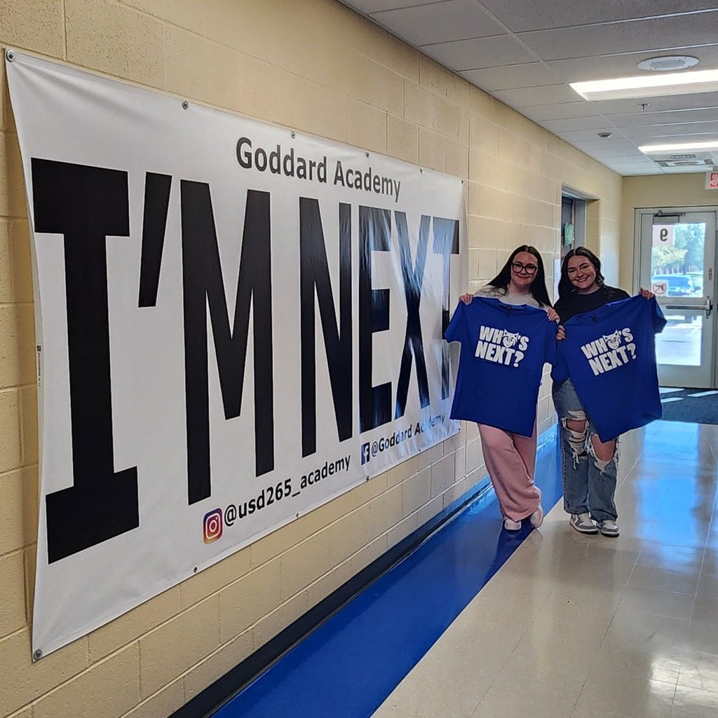 holding "Who's Next "shirt in front of "I'm next "banner 