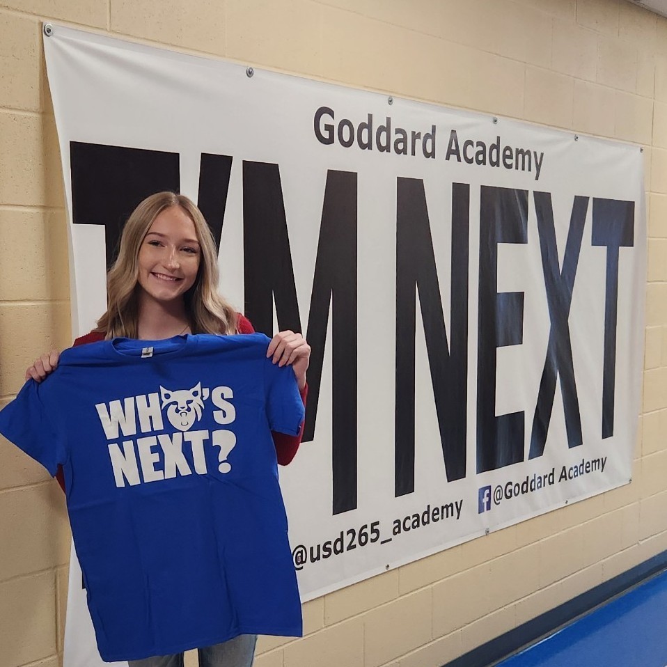holding "Who's Next "shirt in front of "I'm next "banner 