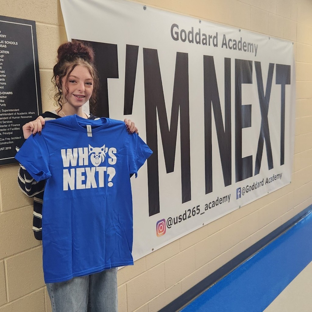 Holding "Who's Next " shirt in front of "I'm next "banner 