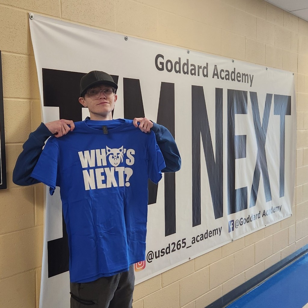 Holding "whos next" shirt in front of "im next" banner