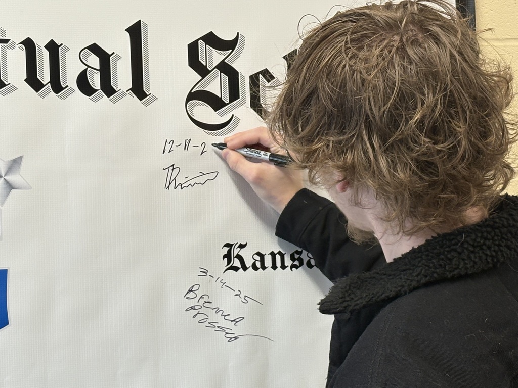 Student signing his name to the graduation poster