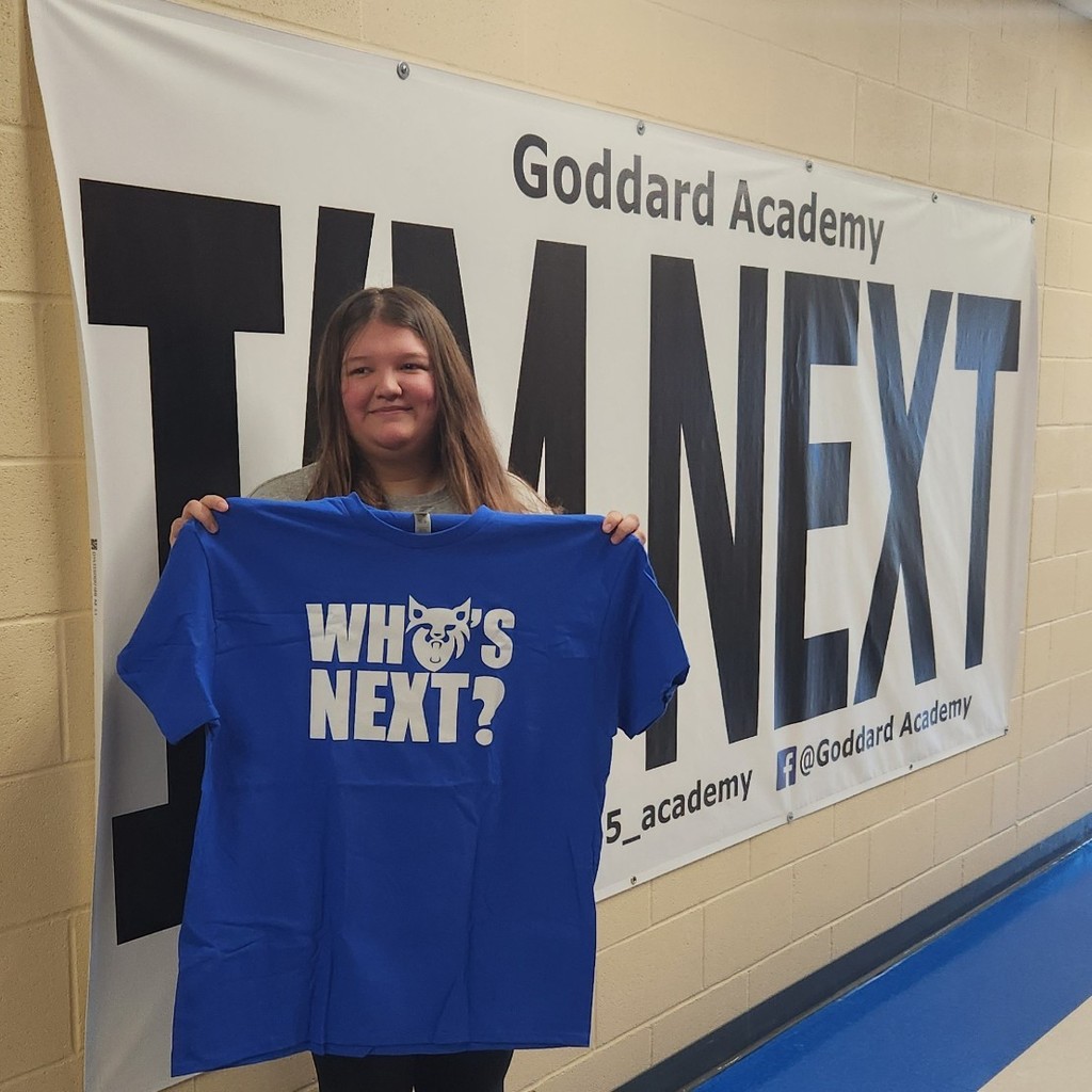 holding "who's next" shirt by "I'm Next" banner