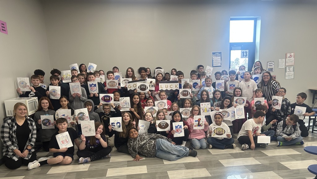 Students gathered in a cafeteria holding up signs decorated for the superbowl to support a fellow student