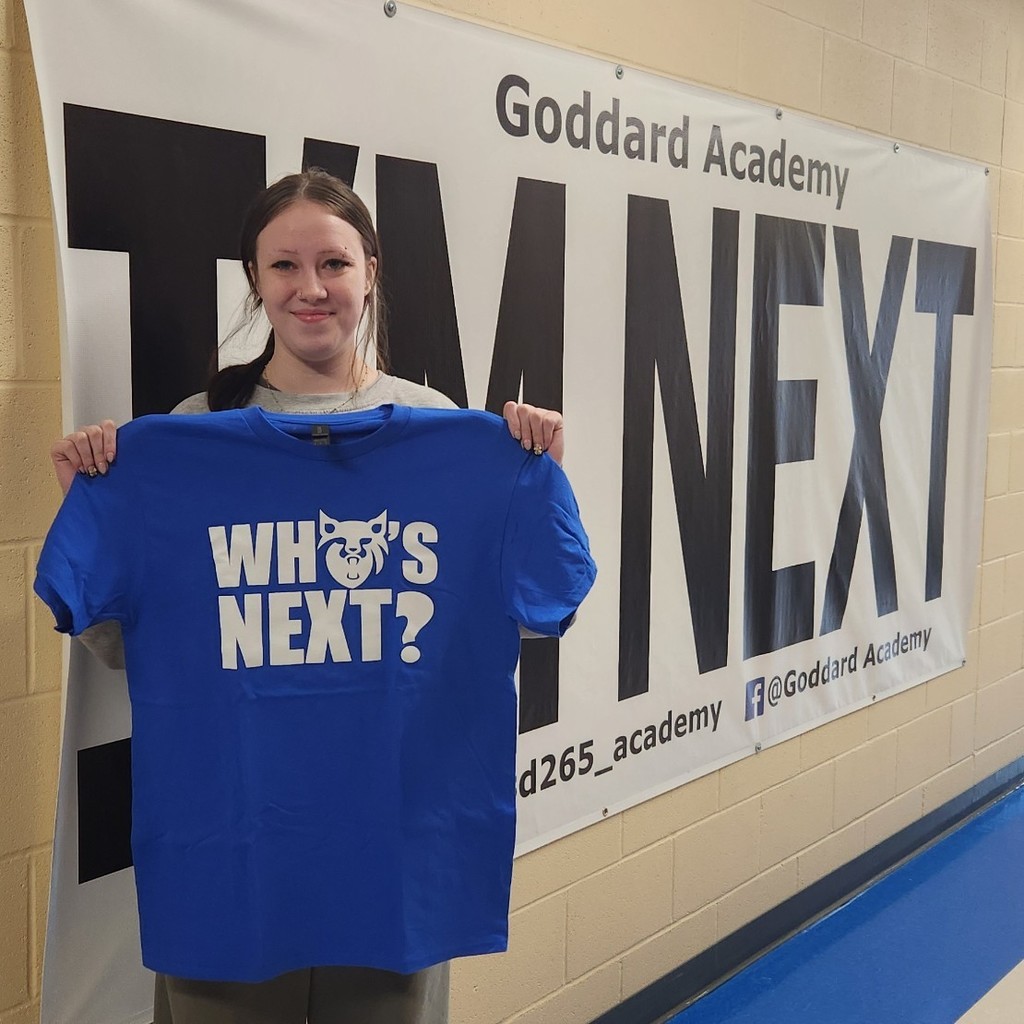 Holding "Who's Next" shirt in front of "I'm next" banner
