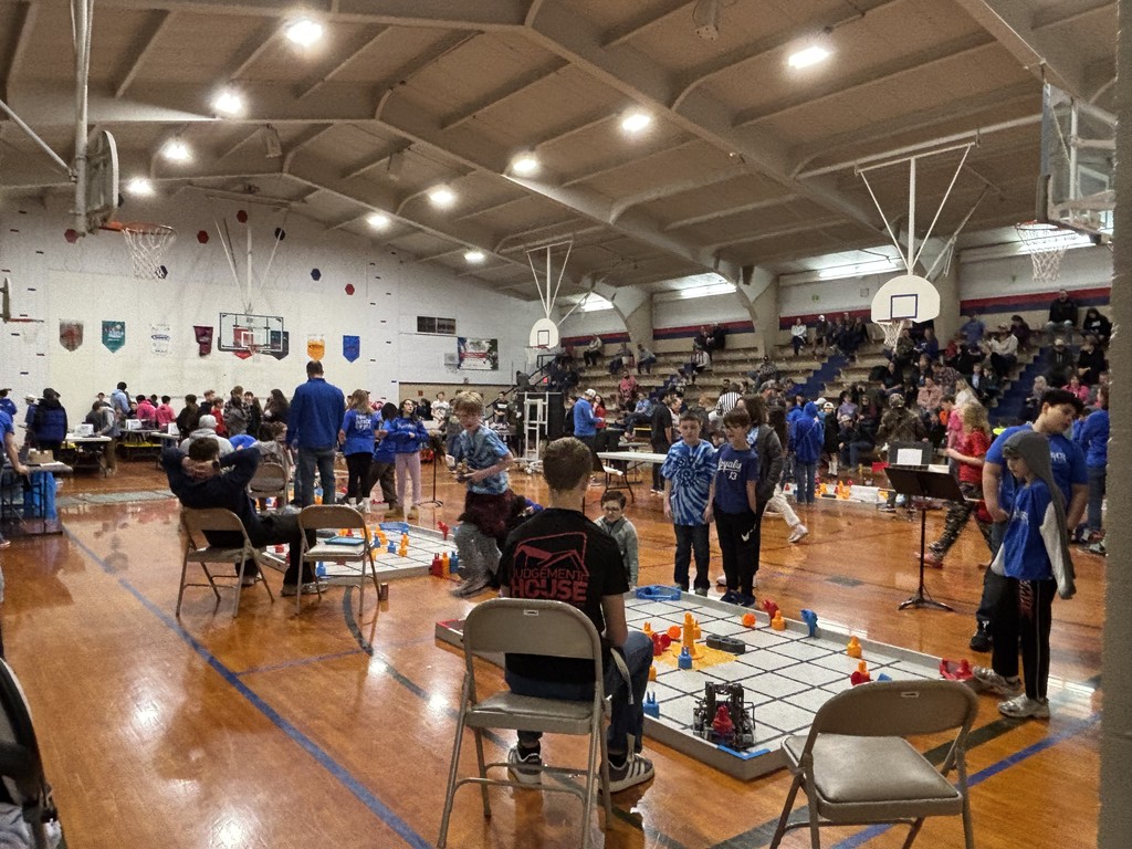 A crowded gym full of kids and adults with robotic boards on the floor.