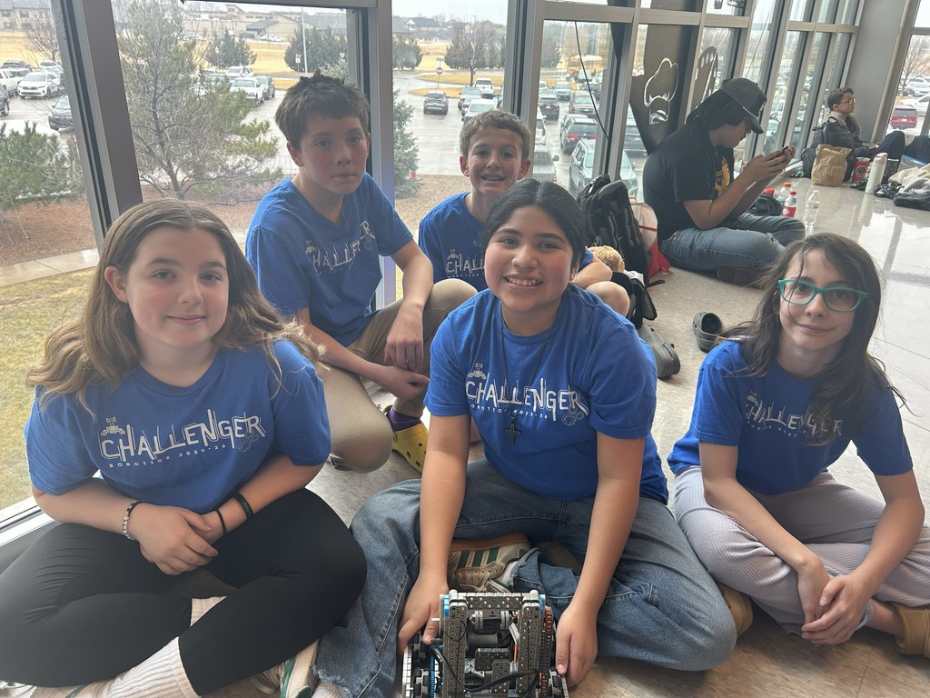 5  Students sitting in a hallway smiling for a picutre. 