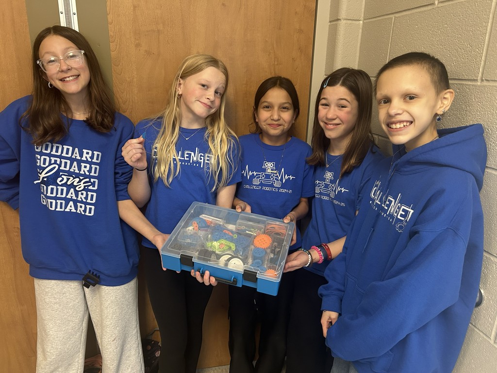 5 students wearing Challenger gear, showing off their robotics items. 
