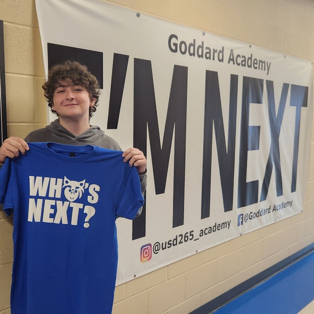 Holding "Who's Next" Shirt in front of Im next banner