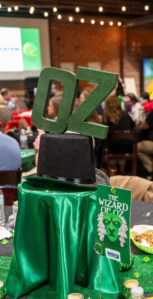 Table centerpiece inspired by "The Wizard of Oz" features a green glitter "OZ" atop a black hat. The tablecloth is green, creating a festive ambiance.