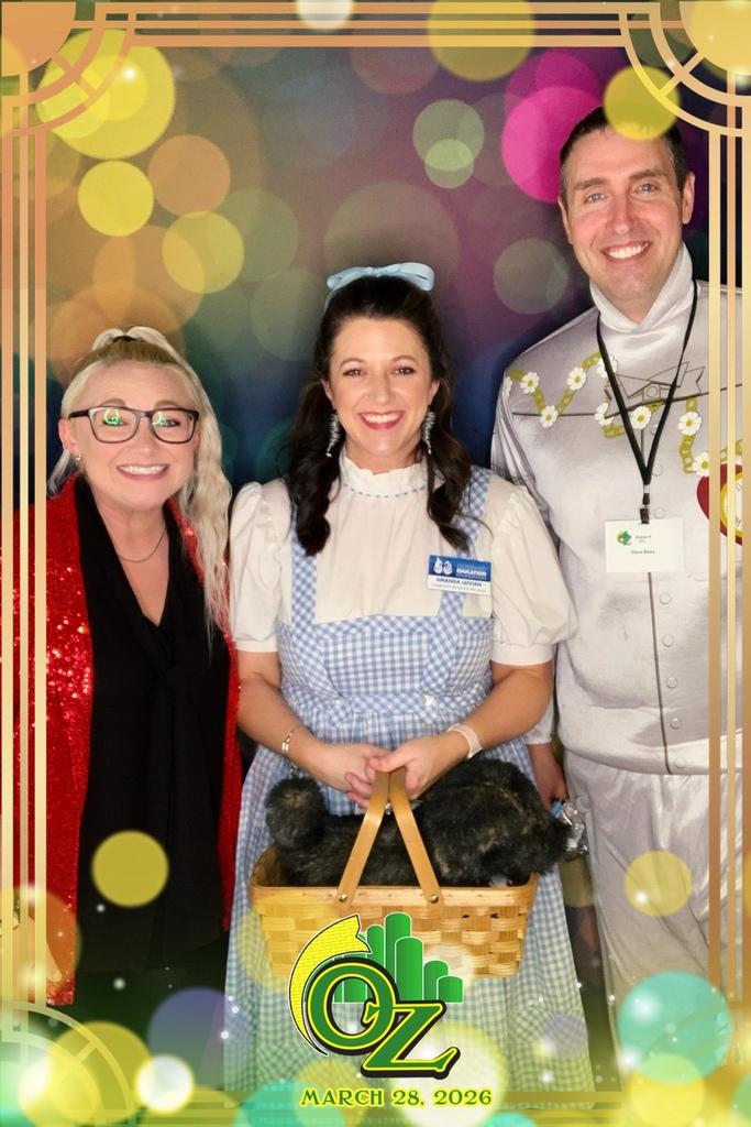 Three people in costume against a colorful bokeh backdrop. One is dressed as Dorothy from "The Wizard of Oz" holding a basket. Smiling faces convey a joyful theme. Text reads "Oz, March 28, 2026."