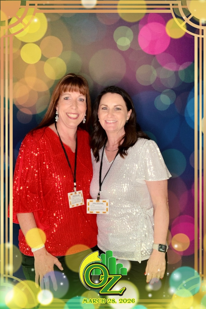 Two women, smiling and posing together. One wears a sparkling red top, the other a silver one. Colorful bokeh lights create a festive backdrop. The frame and text at the bottom read "OZ, March 28, 2026."