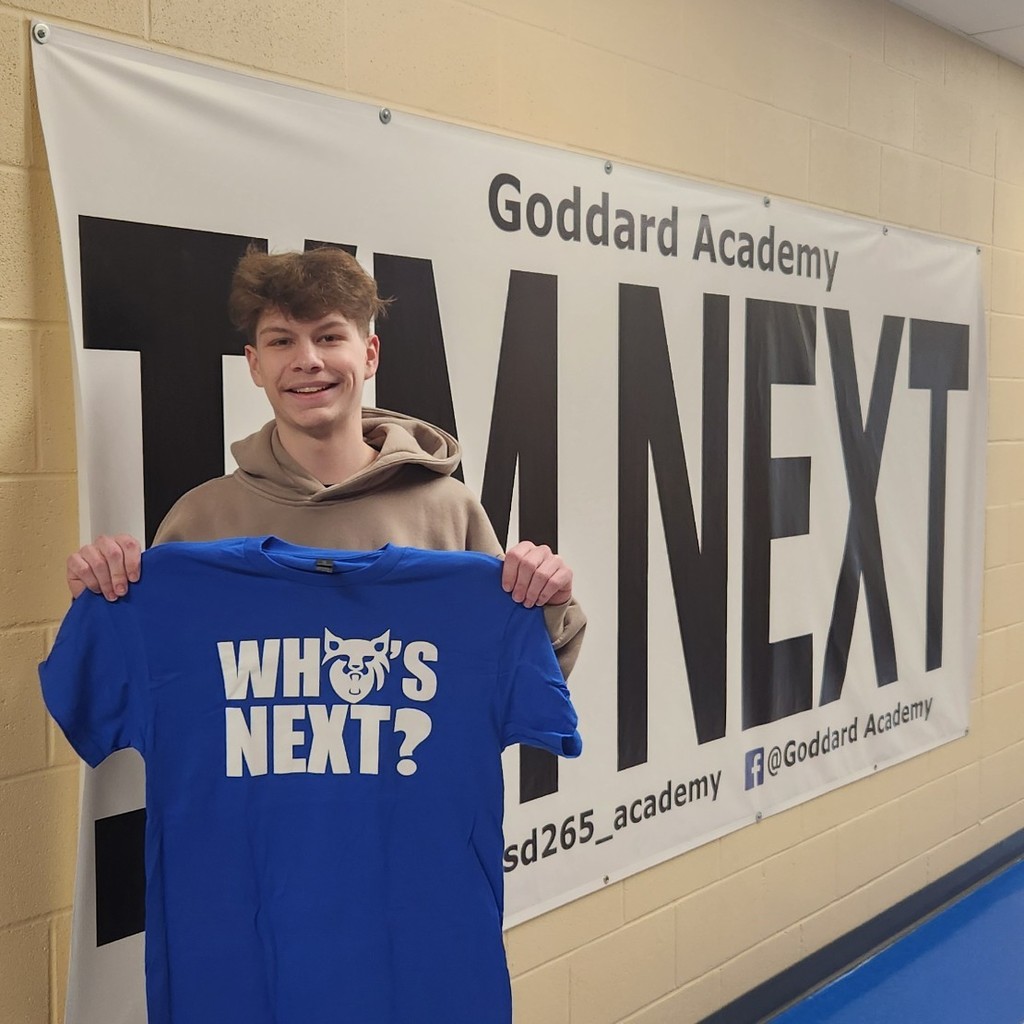 holding "Who's next?" shirt in front of "I'm next" banner