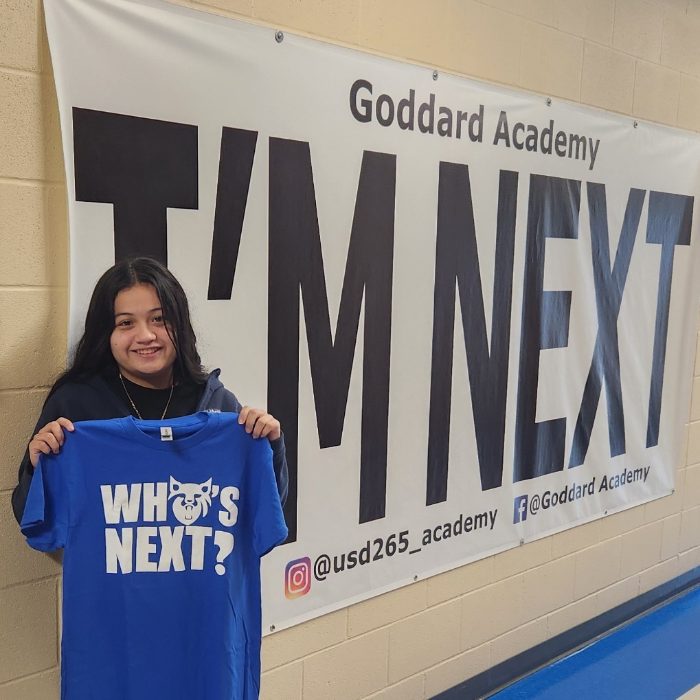 Holding "Who's next" shirt next to "I'm Next" banner