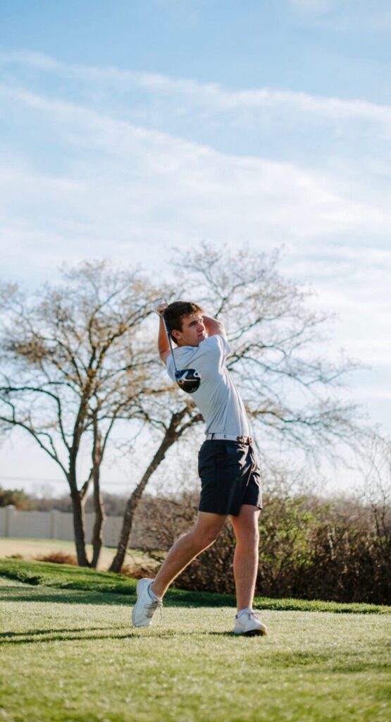 background: green grass, trees, bushes, Jackson Loomis swinging a golf club