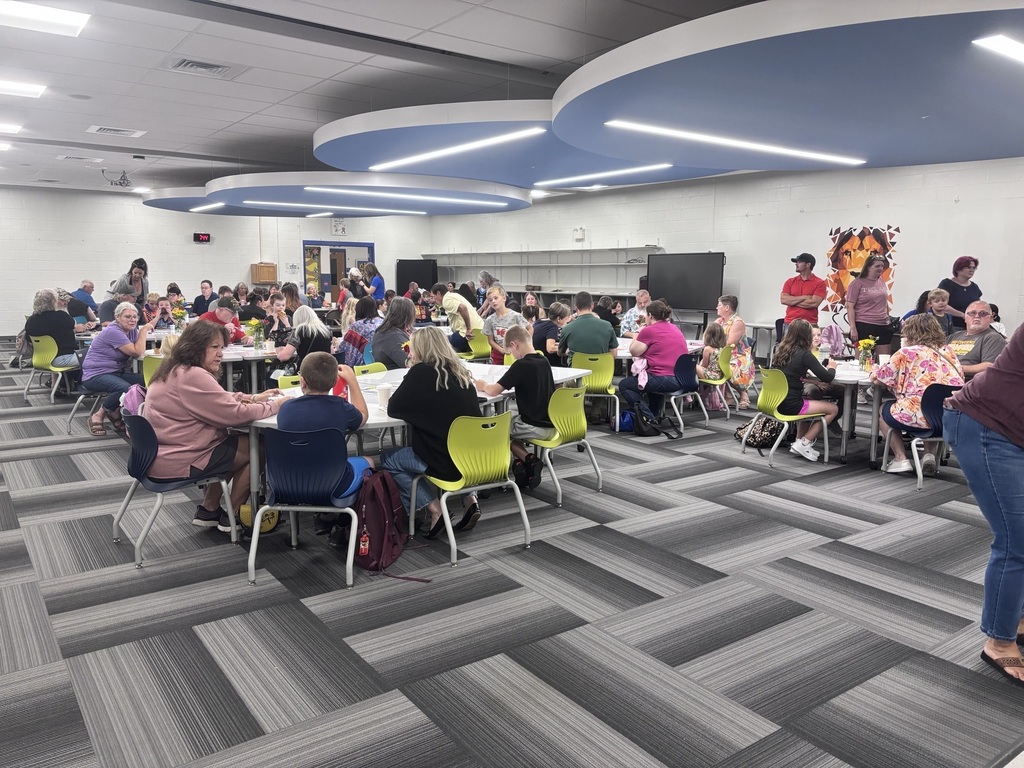 A lively school cafeteria filled with children and adults eating together, colorful chairs, Halloween costumes, and bright modern ceiling lights.