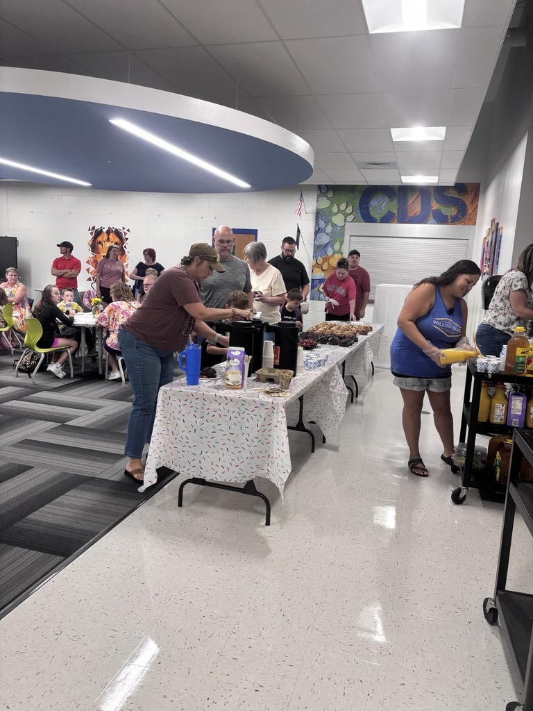 A lively school cafeteria filled with children and adults eating together, colorful chairs, Halloween costumes, and bright modern ceiling lights.