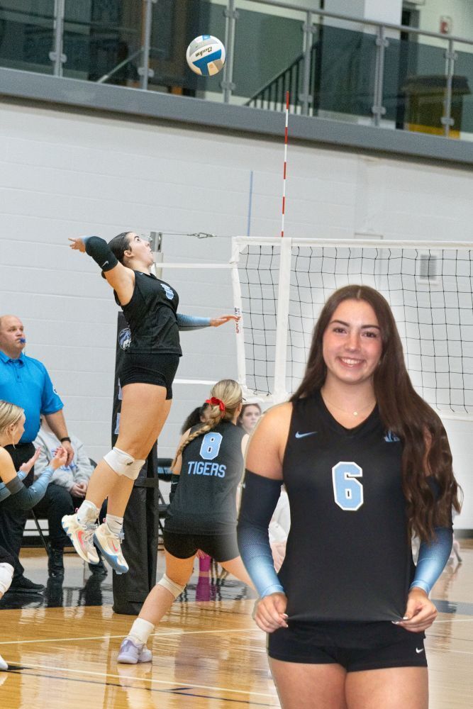 background: volleyball court with a player jumping to spike the ball over the net, photo of #6 Emmarie Barger smiling facing forward