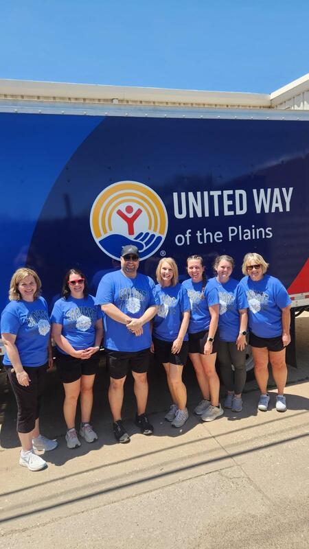 A group of six individuals wearing blue t-shirts stand in front of a United Way of the Plains truck, smiling.