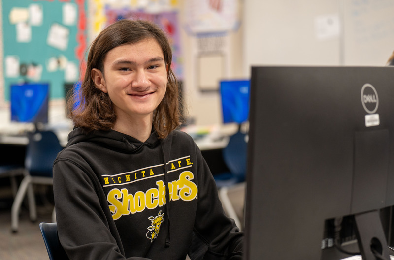 Kevin Kiralyfalvi sitting at a computer, looking at the camera and smiling.
