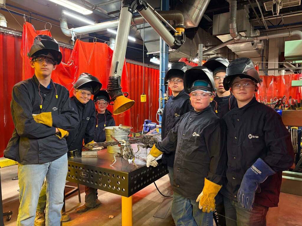 CTE Summer Welding students posing in welding jackets, helmets, and gloves in front of a welding bay
