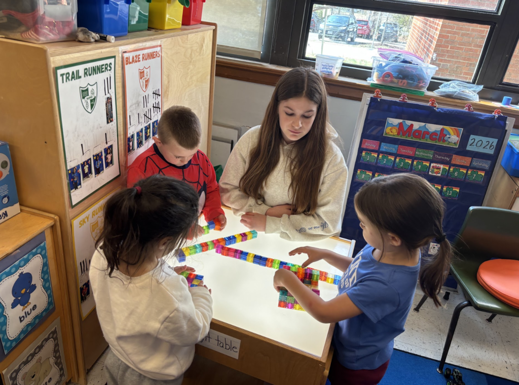 Girl helping helping elementary student build blocks