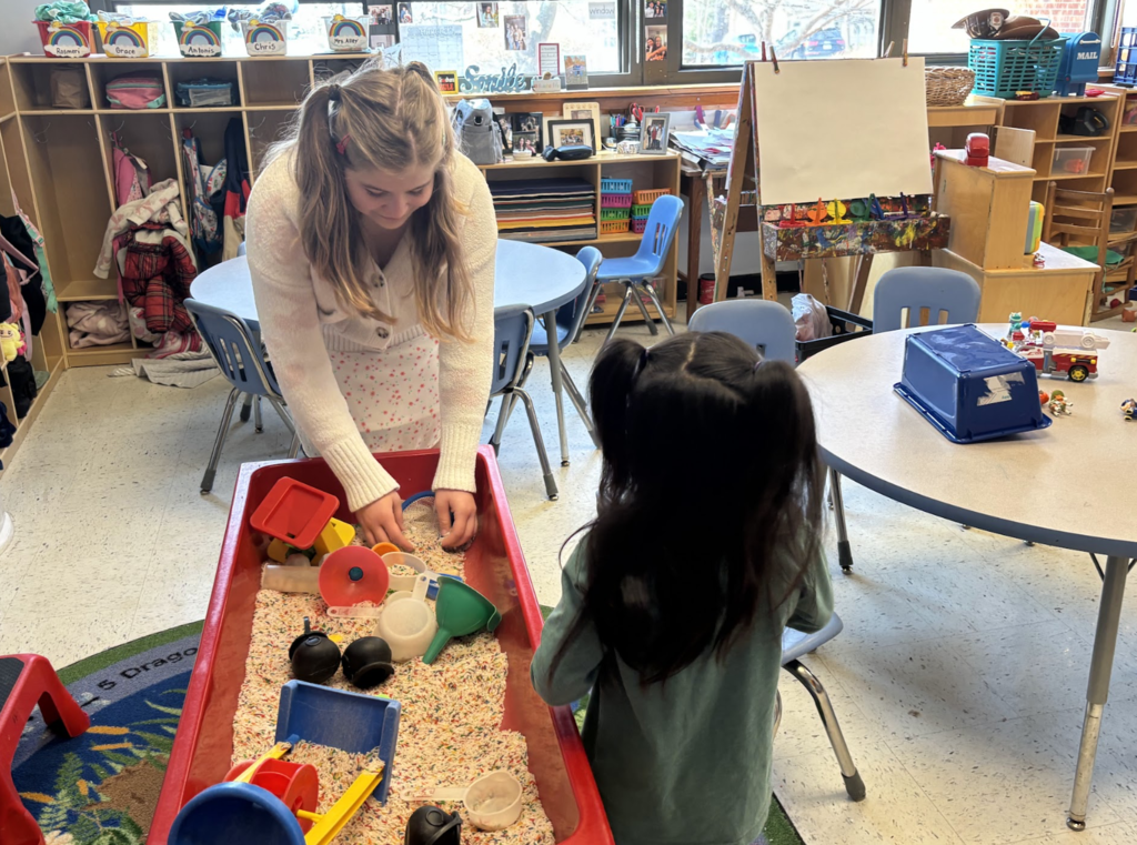 Girl playing with elementary student in sand table