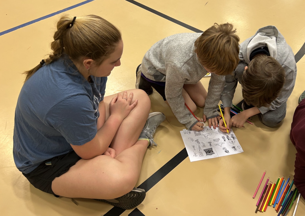 Middle school girl watching two elementary aged boys work on a STEM activity
